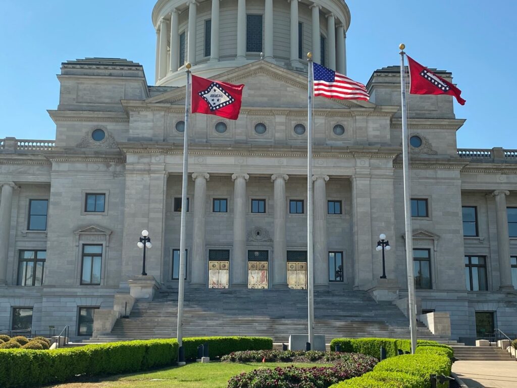 The grand Arkansas State Capitol building in Little Rock with flags waving on a clear, sunny day.