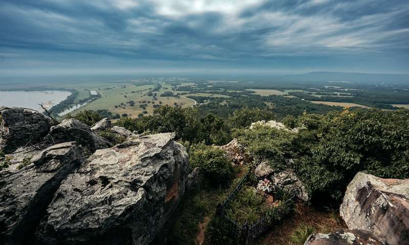 Expansive view from a rocky bluff of lush farmland and winding river in Conway County, Arkansas, captured under a dramatic sky.
